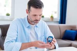 Man sitting, checking his blood glucose level with a digital glucometer.