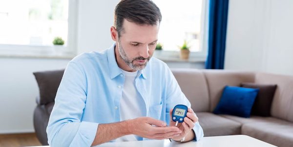 Man sitting, checking his blood glucose level with a digital glucometer.