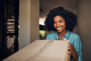 A person with curly hair wearing a denim shirt holding a cardboard box.