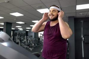 Person in a purple tank top adjusting headphones in a gym with exercise equipment.