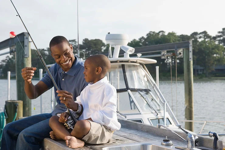 A father and son happily fishing on a boat at the dock.