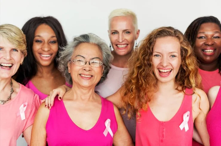 Six women wearing pink and breast cancer awareness ribbons stand together smiling.