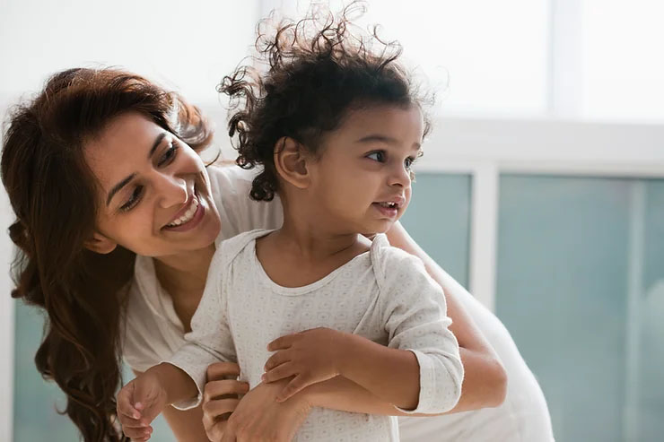 A mother happily holding her toddler, both smiling.