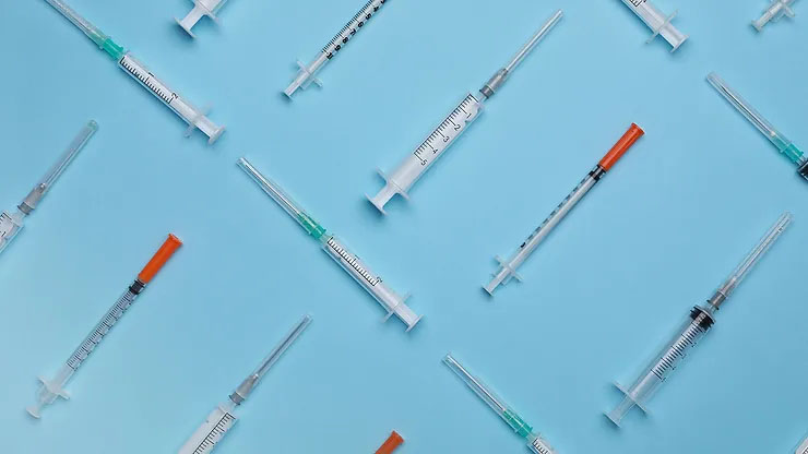 Several disposable syringes arranged in a geometric pattern rest on top of a light blue background.